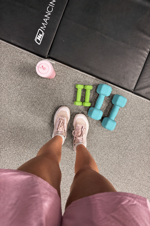 Lime green and light teal dumbbells beside workout shoes on a gym floor